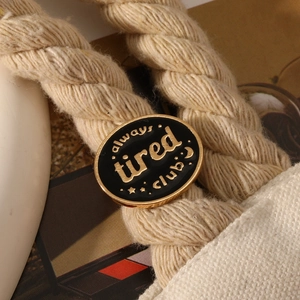Close-up of Always Tired Club enamel pin on a canvas bag handle for style detail