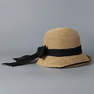 Detailed view of women's straw sun hat featuring black ribbon trim and pearl accents