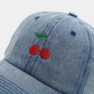 Macro detail of high-quality red cherry embroidery on a blue denim baseball cap surface