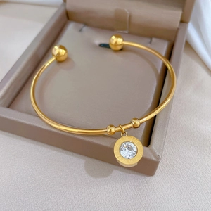 Detail of a gold cuff bracelet with a Roman numeral charm and a sparkling zircon stone