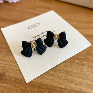 Macro detail of matte black bow earrings with gold center on a display card