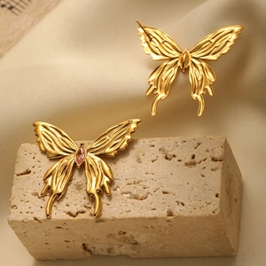 Macro shot of 3D butterfly gold earrings with pink gemstones on natural stone