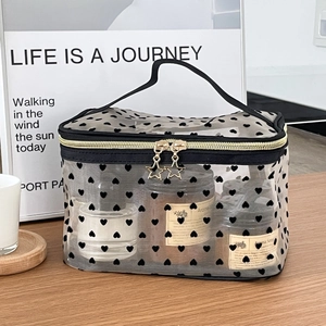 Portable black mesh heart makeup bag with golden star zipper and top handle on wooden table