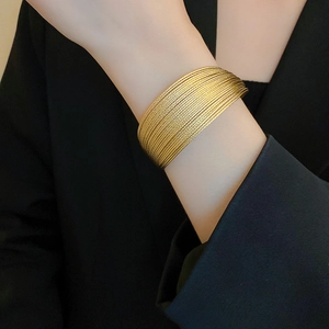 Close-up of layered gold metal cuff bracelet with textured finish worn on black suit sleeve