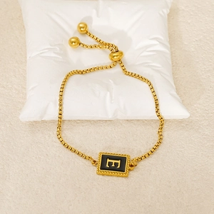 Detail view of golden chain bracelet with black enamel rectangle pendant featuring letter E