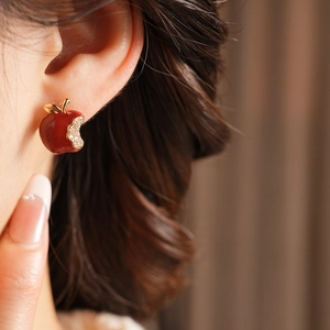 Detailed close-up of a red enamel apple earring with sparkling crystals on gold metal