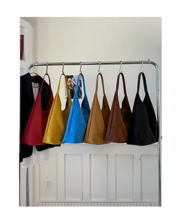 Multiple colorful vintage suede tote bags in red yellow blue and brown hanging on a rack