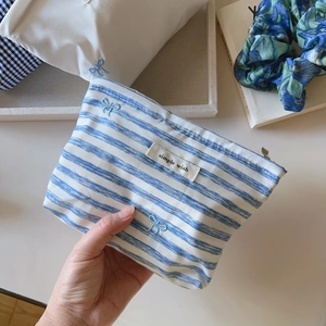 Detail of blue striped canvas makeup bag with bow embroidery and zipper closure