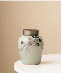 Close-up of light green crackle glaze ceramic jar with pink floral patterns and metal lid