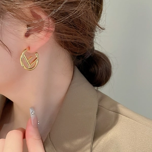 Close-up of golden letter C-shaped earrings with hollow F design on model ear