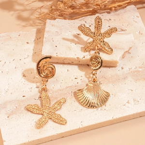 Close-up of asymmetric gold starfish and seashell earrings on a natural stone base