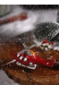 Detail shot of a red helicopter Christmas ornament on a rustic wood slice with snow and pine