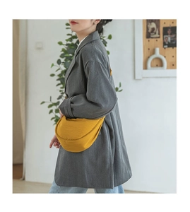 Side view of a yellow canvas crescent crossbody bag worn with a casual grey blazer