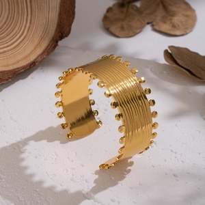 Macro detail of gold ripple textured wide cuff bracelet with beaded edges on stone background