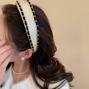 Close-up of a white padded headband with woven gold metal chain and black velvet ribbon