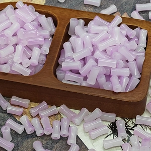 Macro shot of lavender gradient glass bamboo joint beads in a wooden tray for DIY