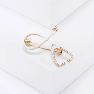 Detailed view of stethoscope brooch with gold metal and white enamel on a clean backdrop