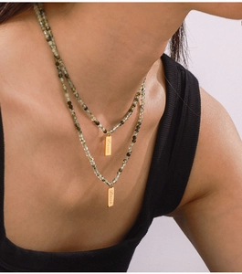 Detail of layered green beaded necklace featuring golden pendants with Love engraving
