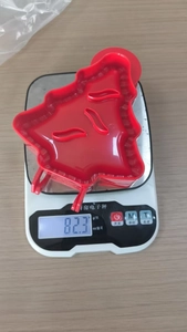 Detailed view of a red 3D Christmas tree cookie mold being weighed on a kitchen scale