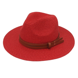 Close-up of red woven straw fedora hat with brown leather band and metal rivets detail