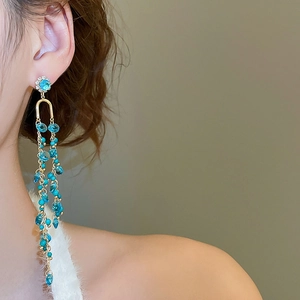 Close-up of elegant long tassel earrings with blue gemstones and gold chain on a model
