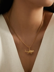 Detail of shark pendant necklace in 18k gold plated stainless steel on a white knit V-neck