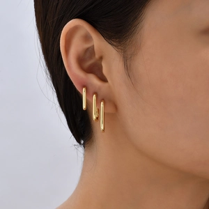 Close-up of three layered gold rectangular hoop earrings on a female model ear