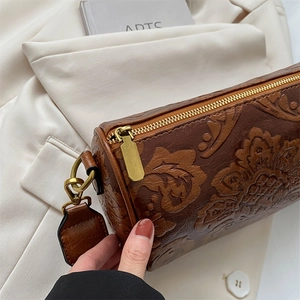 Detailed close-up of brown embossed leather floral cylinder bag with retro bronze metal hardware