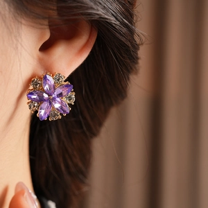 Macro di orecchini a fiore in oro con petali di cristallo viola e piccoli diamanti