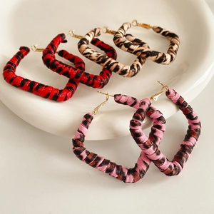 Three pairs of woven leopard print hoop earrings in red, brown, and pink on a white plate