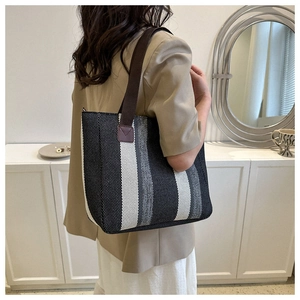 Detail of striped canvas tote bag with brown shoulder strap worn by a person