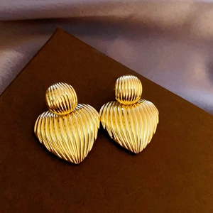 Macro shot of gold-plated ribbed metal heart earrings with vertical textured details