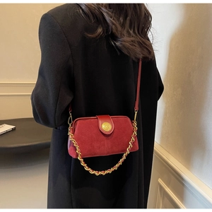 Detail of burgundy suede shoulder bag with gold chain strap on a black coat