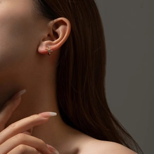 Close-up of elegant gold flower stud earrings with blue and white zircon on ear