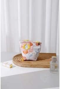Detail of floral makeup bag with orange embroidery and yellow tassel on a wooden tray