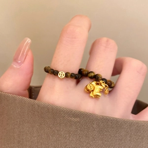Detail of tiger eye bead ring with gold-plated Pixiu and coin charms on a hand