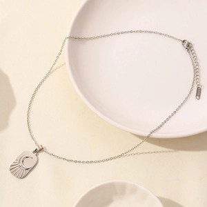 Detail of silver stainless steel moon necklace pendant with sunburst texture on a white tray