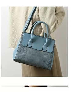 Close-up of grey-blue handbag featuring smooth and crocodile pattern leather texture