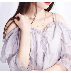 Collier minimaliste en or avec pendentif barre et zircons porté par un mannequin