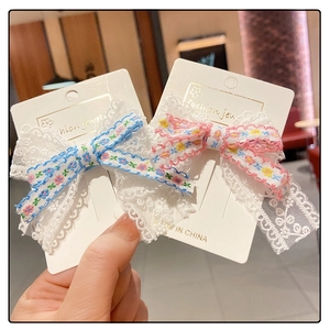 Detail of floral lace bow hair clips in blue and pink on a white jewelry display card
