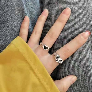 Detail shot of silver rings with black heart and cartoon face design on fingers