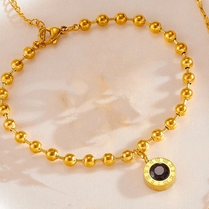 Detail of gold bead bracelet with black stone pendant featuring Roman numeral engraving