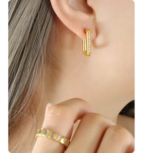 Détail de boucles d'oreilles rectangles en zircon doré et bague assortie portées par un mannequin