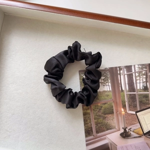 Close-up of black satin scrunchie with glossy pleated texture on a clean white background