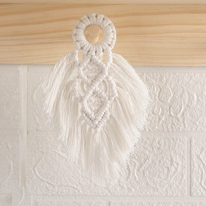 Detail of white cotton macrame feather wall hanging on a rustic wooden hook