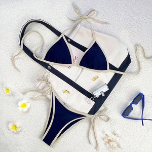Two-piece navy blue bikini with beige trim, halter neck top and side-tie bottoms on beach mat