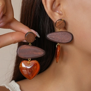 Close-up of heart-shaped resin and wooden drop earrings worn by a model in natural light