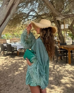Détail de l'ensemble pailleté vert avec bordure en plumes et chapeau de paille