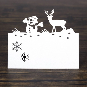Laser-cut white paper place cards with snowman and reindeer designs on dark wood background