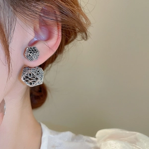 Close-up of silver hollow geometric floral earrings worn by a model in soft light